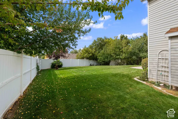Spacious side yard featuring a manicured lawn, white vinyl fencing, and mature trees