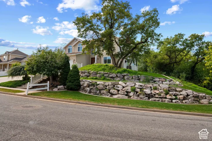 View of front of house featuring natural stone tiered retaining walls, and mature trees