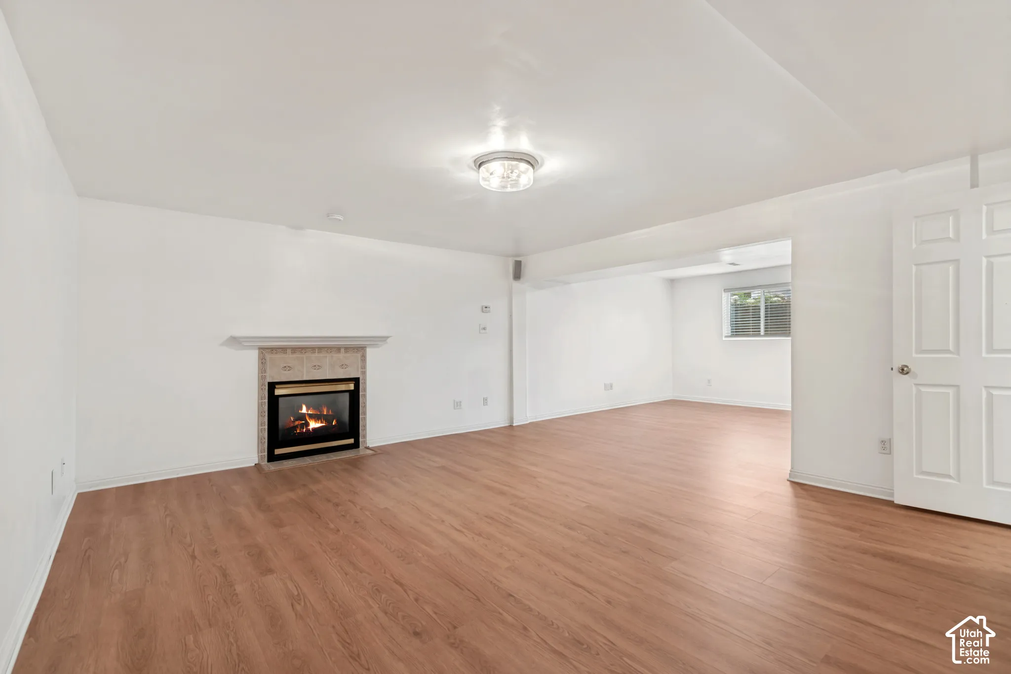 Interior space featuring wood-finish flooring, a fireplace with a decorative tile surround and mantel, a ceiling-mounted flush light fixture, and a six-panel door