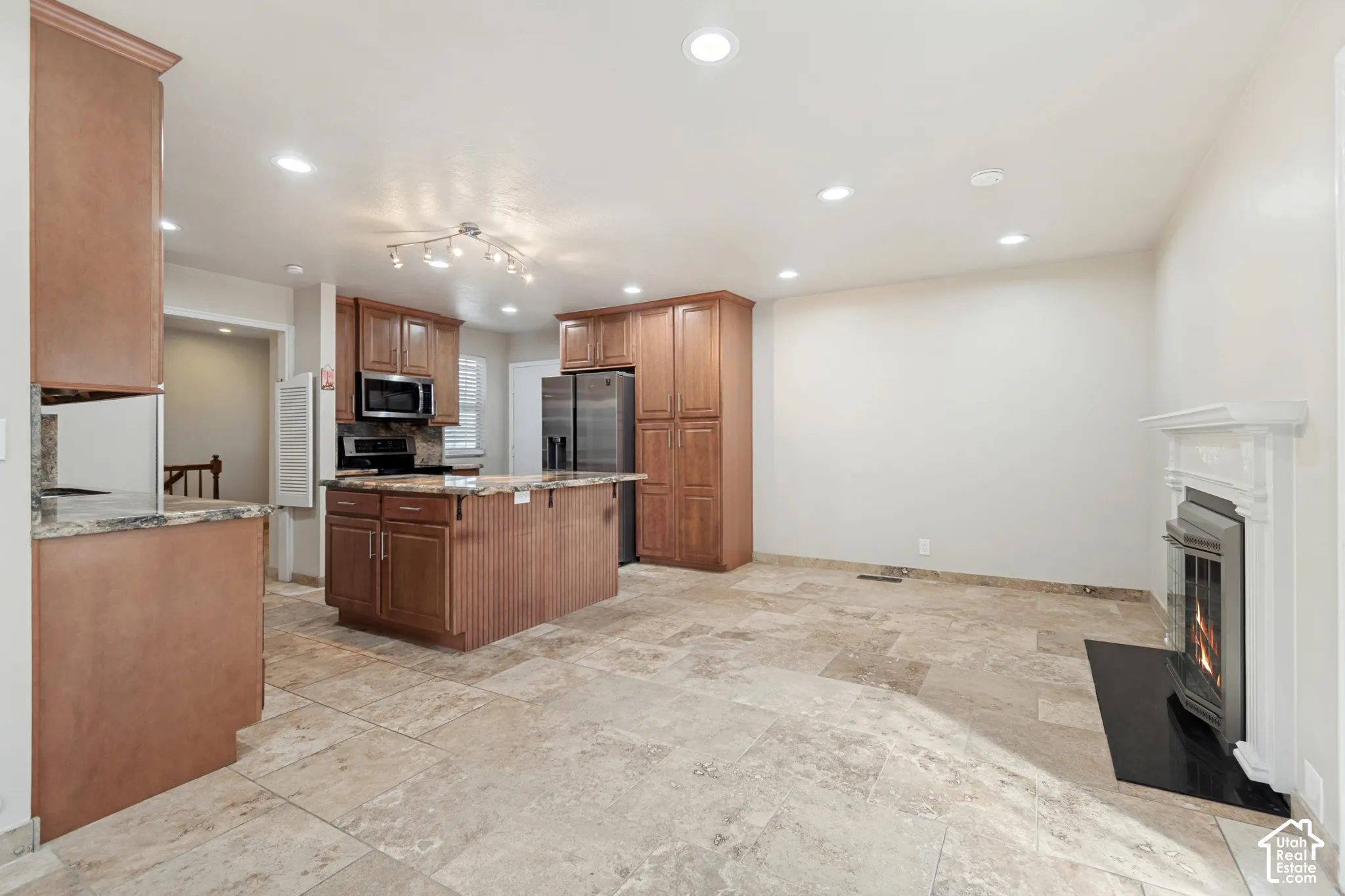 Kitchen featuring wood cabinetry, stone countertops, central island, natural stone flooring, and a fireplace with a decorative mantel