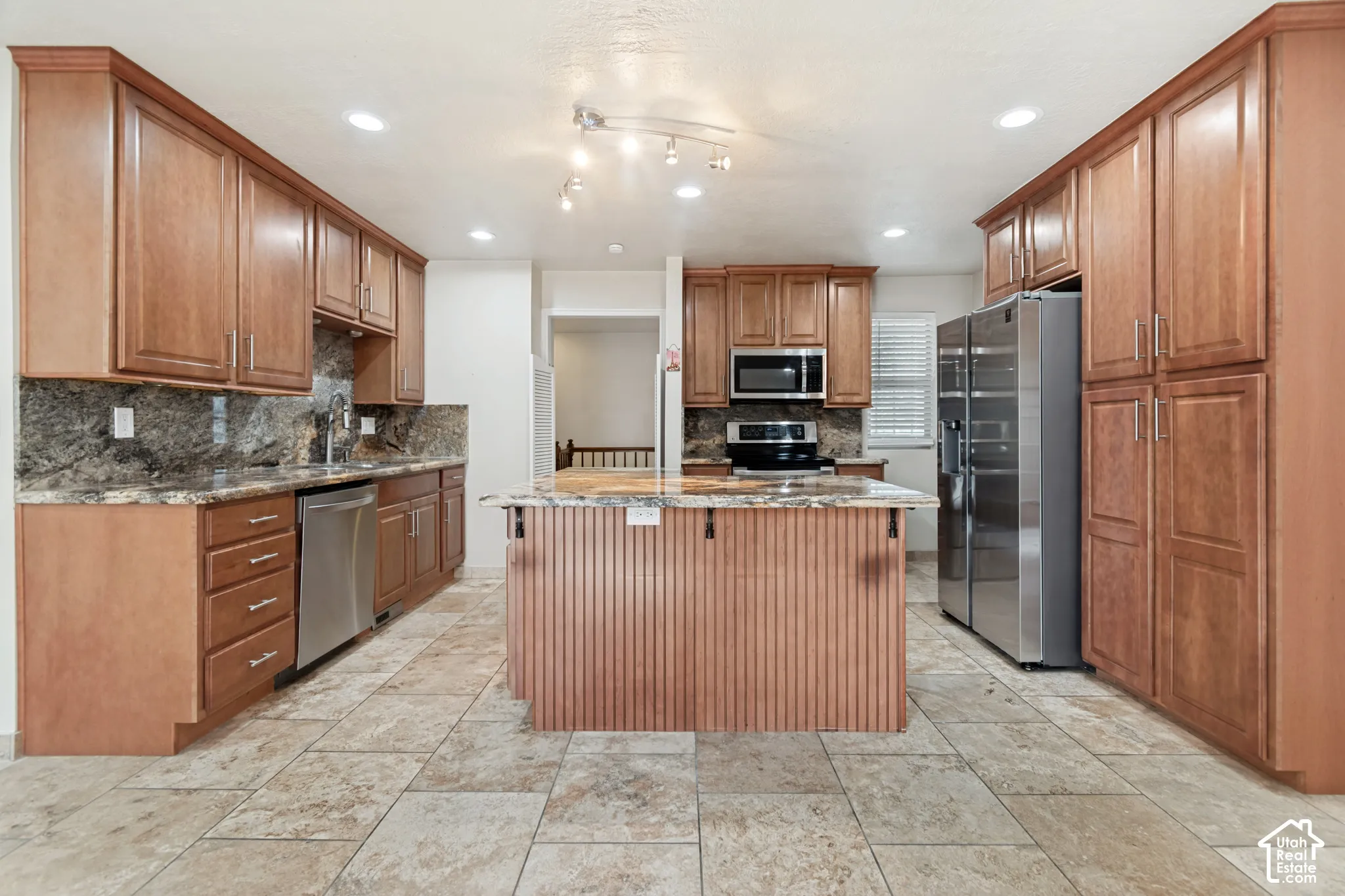 Kitchen featuring extensive wood cabinetry, stone-finish countertops, center island with beadboard detailing, stainless steel appliances, and tiled flooring