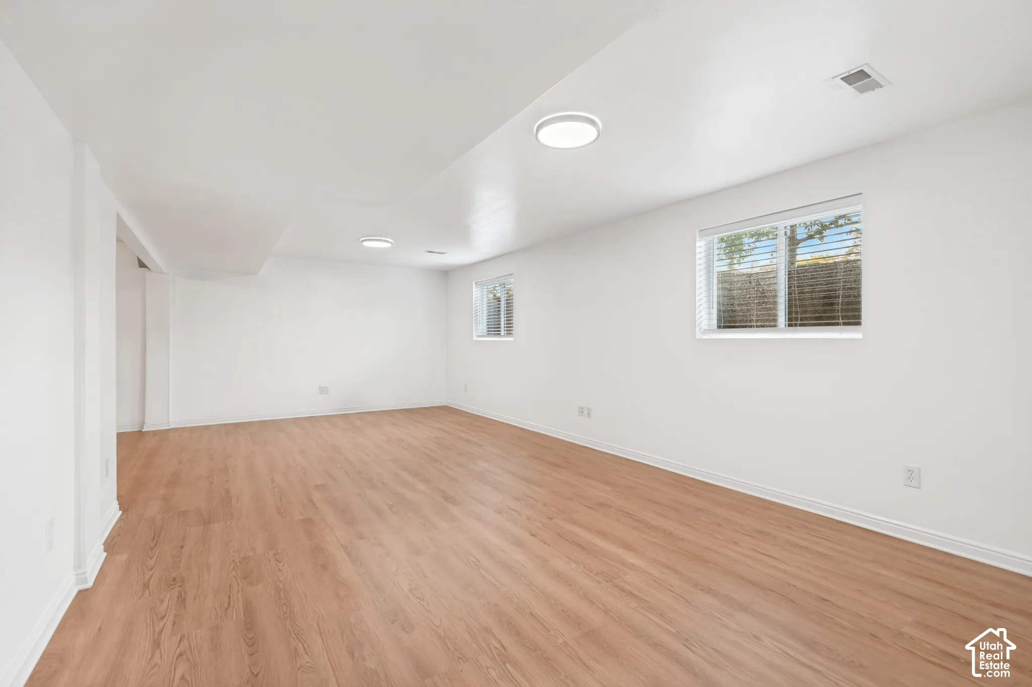Neutral interior space featuring wood-finish flooring, crisp white walls, and dual flush-mount ceiling light fixtures