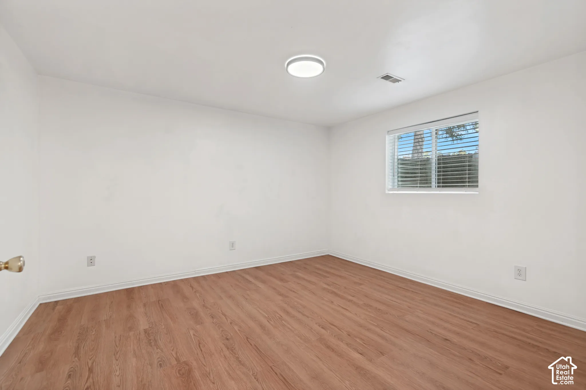 Room featuring wood-finish flooring, white walls, a flush-mount circular light fixture, and a sliding window with horizontal blinds