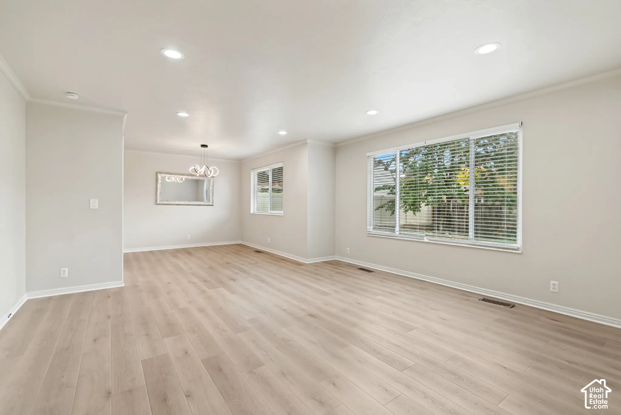 Open-concept interior featuring light-toned wood-finish flooring, recessed lighting, neutral wall paint, and multi-pane windows with horizontal blinds