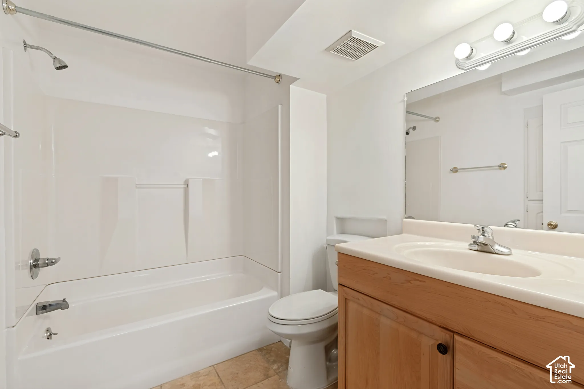 Bathroom featuring a wood-finish vanity with a molded countertop, integrated oval basin, tub-and-shower combination with a surround, and a wall-mounted vanity light