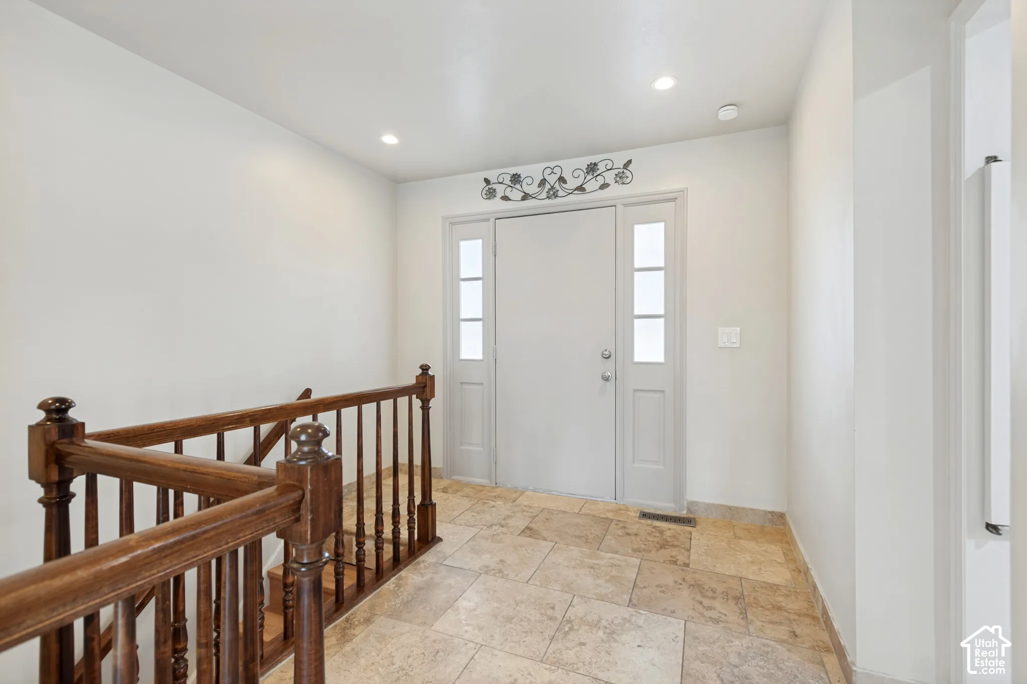 Entryway featuring tile flooring, a solid panel front door with dual glass sidelights, and a wood-finish staircase railing with turned balusters