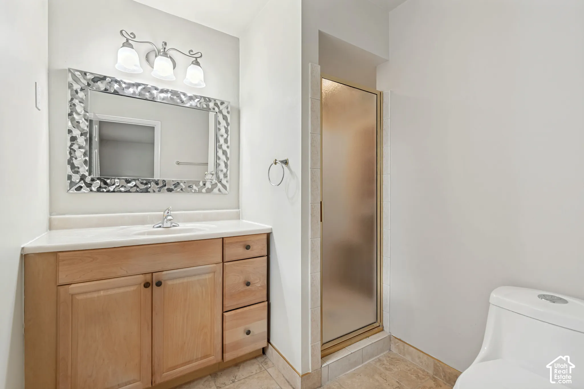 Bathroom featuring a wood-finish vanity with a light-tone countertop, three-light fixture, enclosed glass shower, and tile flooring