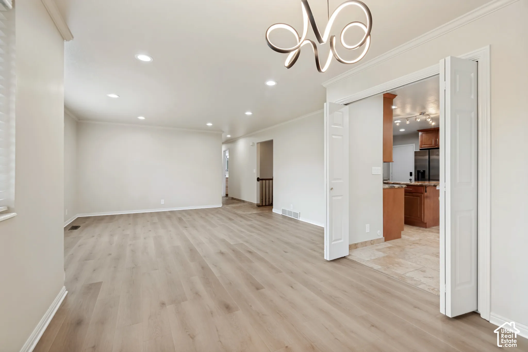 Open-concept interior featuring wood-finish flooring, recessed lighting, a modern sculptural chandelier, and white bi-fold doors