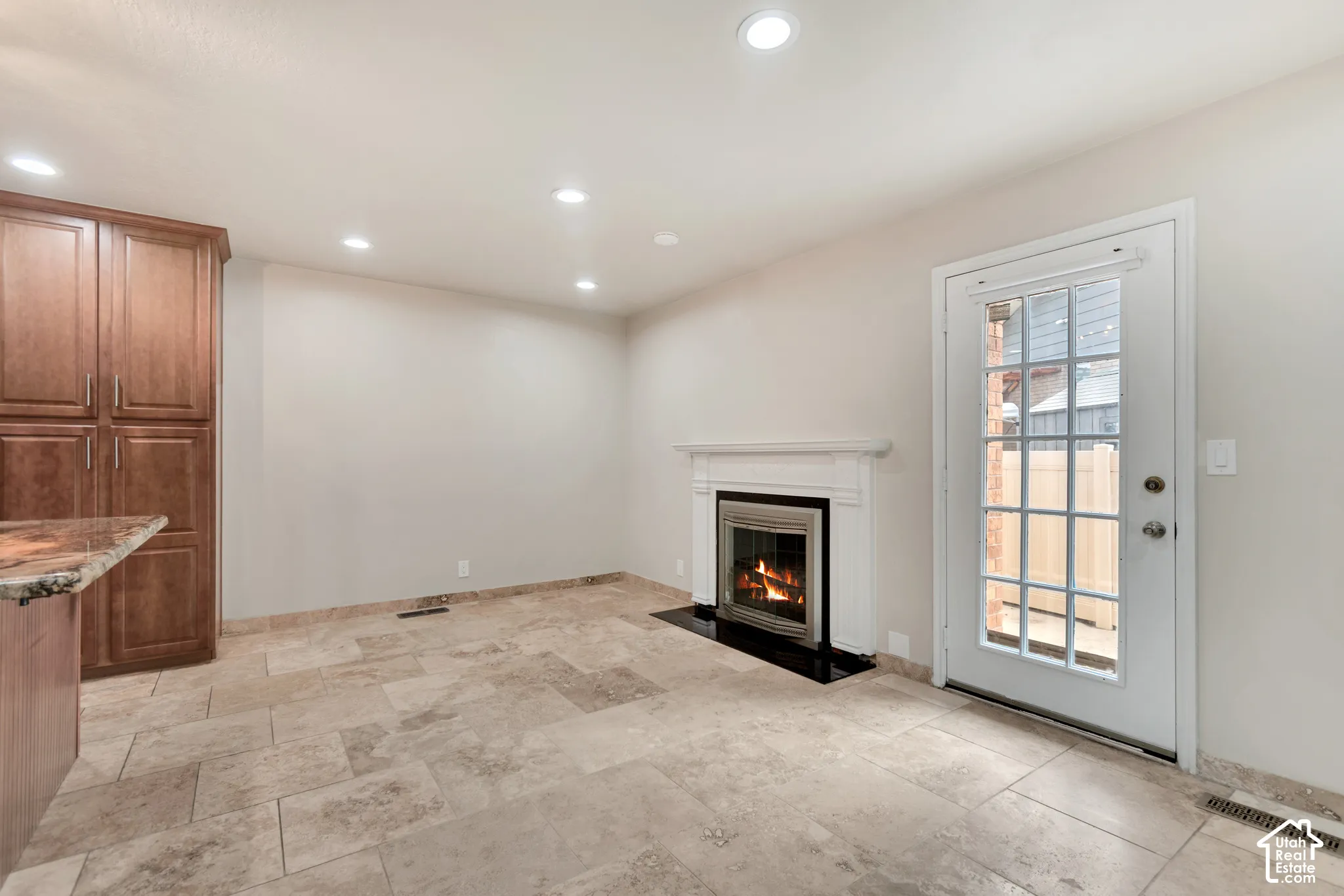 Stone-tiled flooring, wood-finish floor-to-ceiling cabinetry, fireplace with a white mantel and black hearth, and a multi-pane glass door