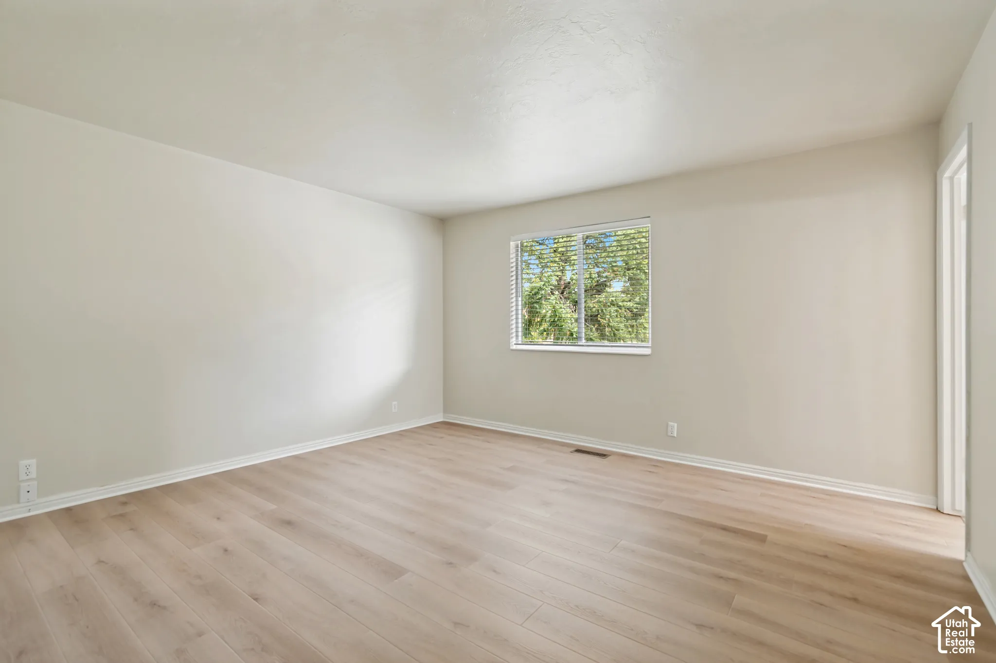 Neutral-toned interior space featuring wood-finish flooring, smooth wall surfaces, and a sliding window