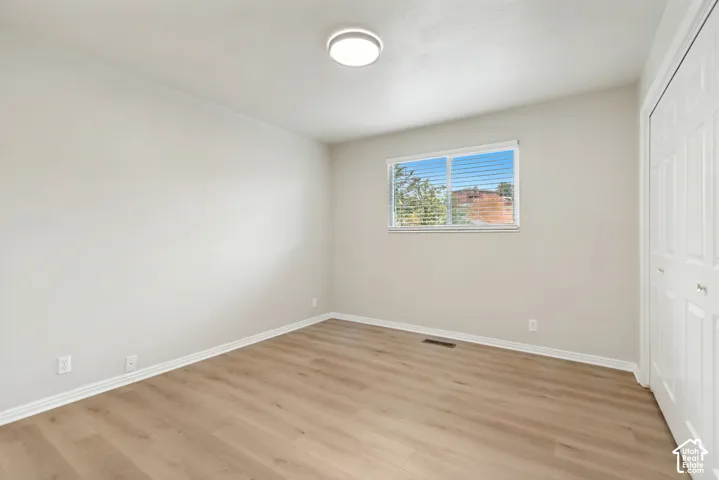 Neutral-toned interior featuring wood-finish flooring, a sliding window, and a built-in double-door closet with a flush-mount ceiling light fixture