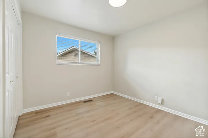 Neutral-toned room featuring wood-finish flooring, a double-door closet, a single window, and a flush-mount ceiling light fixture