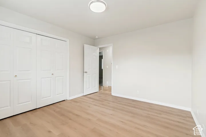 Room featuring neutral wall paint, wood-finish flooring, white bi-fold closet doors, a white interior door, and a circular flush-mount ceiling light