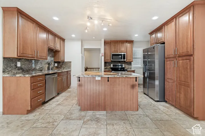 Kitchen featuring extensive wood cabinetry, stone-finish countertops, center island with beadboard detailing, stainless steel appliances, and tiled flooring