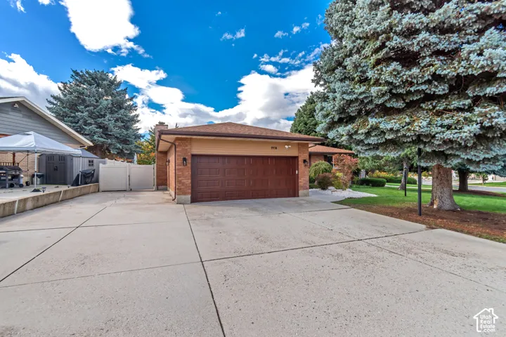 Brick exterior garage featuring a concrete driveway, attached two-car door, hip roofline, and established landscaping