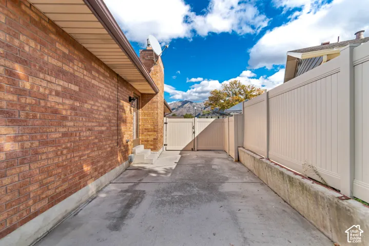 Exterior side yard featuring brick siding, a concrete patio, vinyl privacy fencing, and a concrete retaining wall
