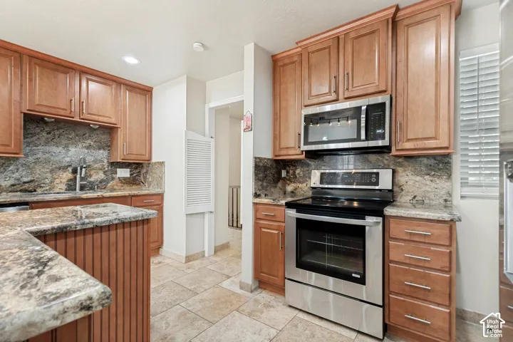 Kitchen featuring natural wood cabinetry, stone countertops, stone tile backsplash, stainless steel appliances, and ceramic tile flooring