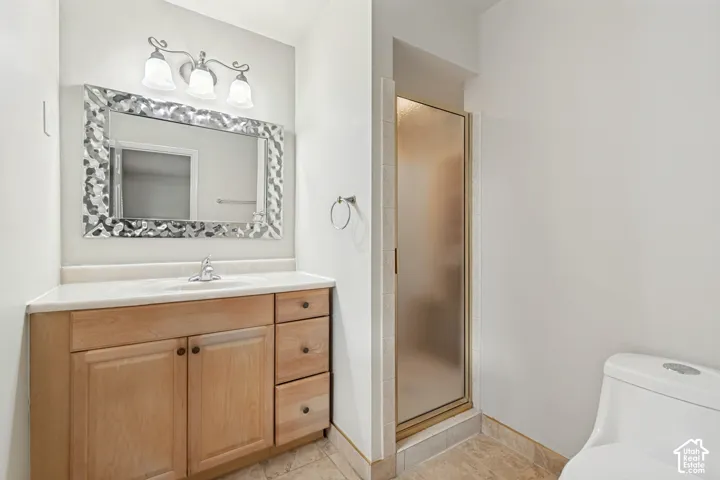 Bathroom featuring a wood-finish vanity with a light-tone countertop, three-light fixture, enclosed glass shower, and tile flooring