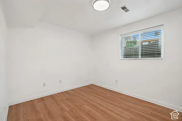 Interior room featuring wood-finish flooring, white walls, and a window with horizontal blinds