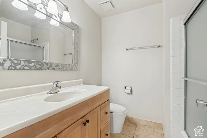 Bathroom featuring a wood-finish vanity with a molded countertop, framed wall mirror, multi-bulb light fixture, and a glass-enclosed shower