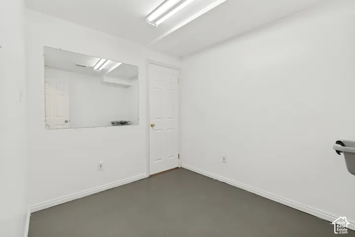 Neutral-toned room featuring a six-panel interior door, wall-mounted rectangular mirror, and overhead fluorescent lighting