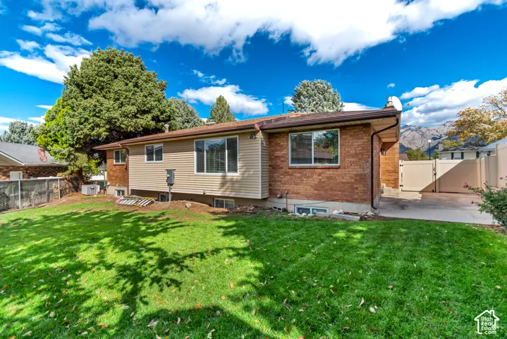 Exterior featuring a brick and vinyl siding facade, a manicured lawn, mountain backdrop, and concrete hardscaping