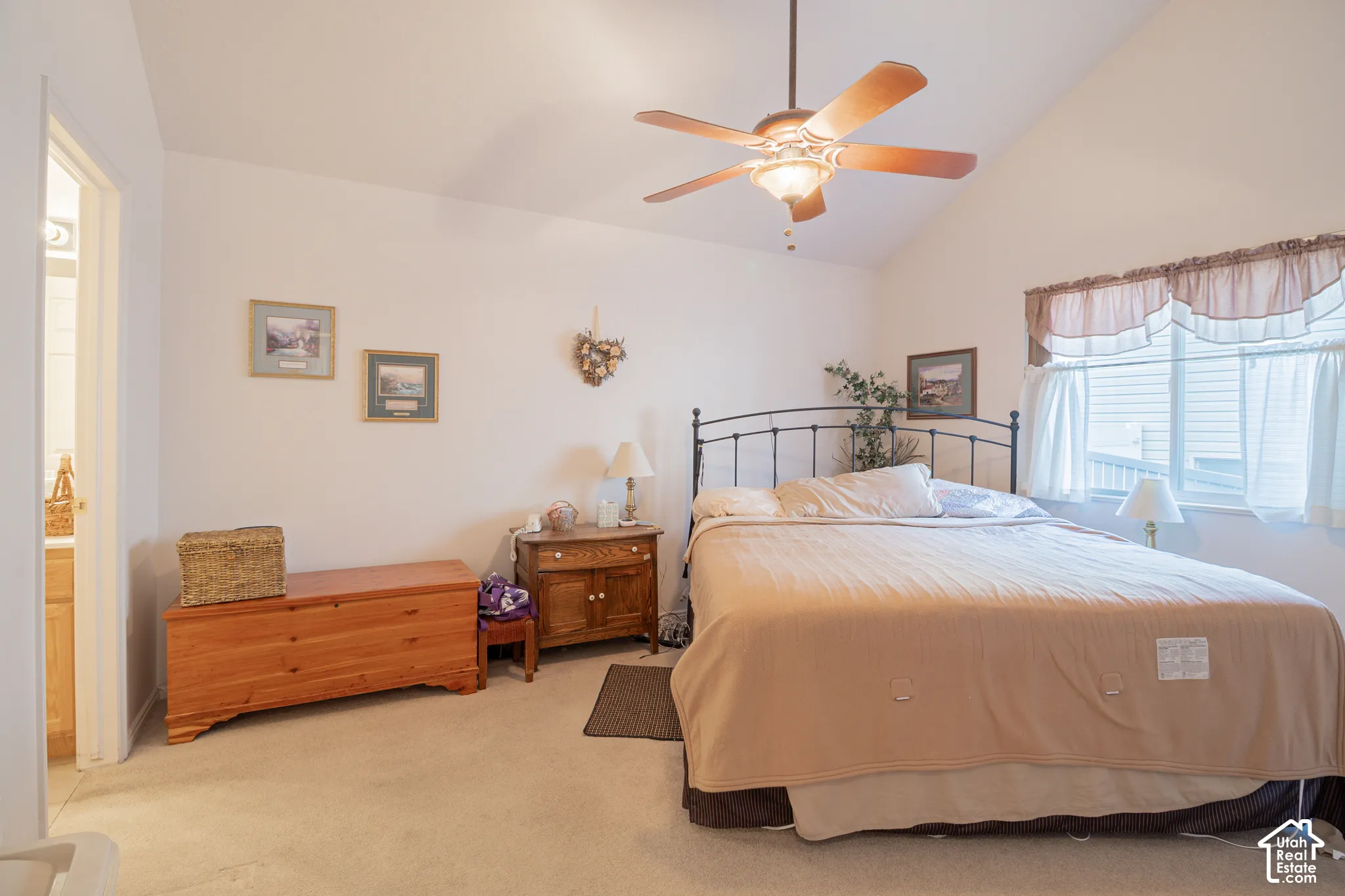 Vaulted ceilings featuring a central ceiling fan with integrated lighting, neutral wall-to-wall carpeting, and a window with a valance