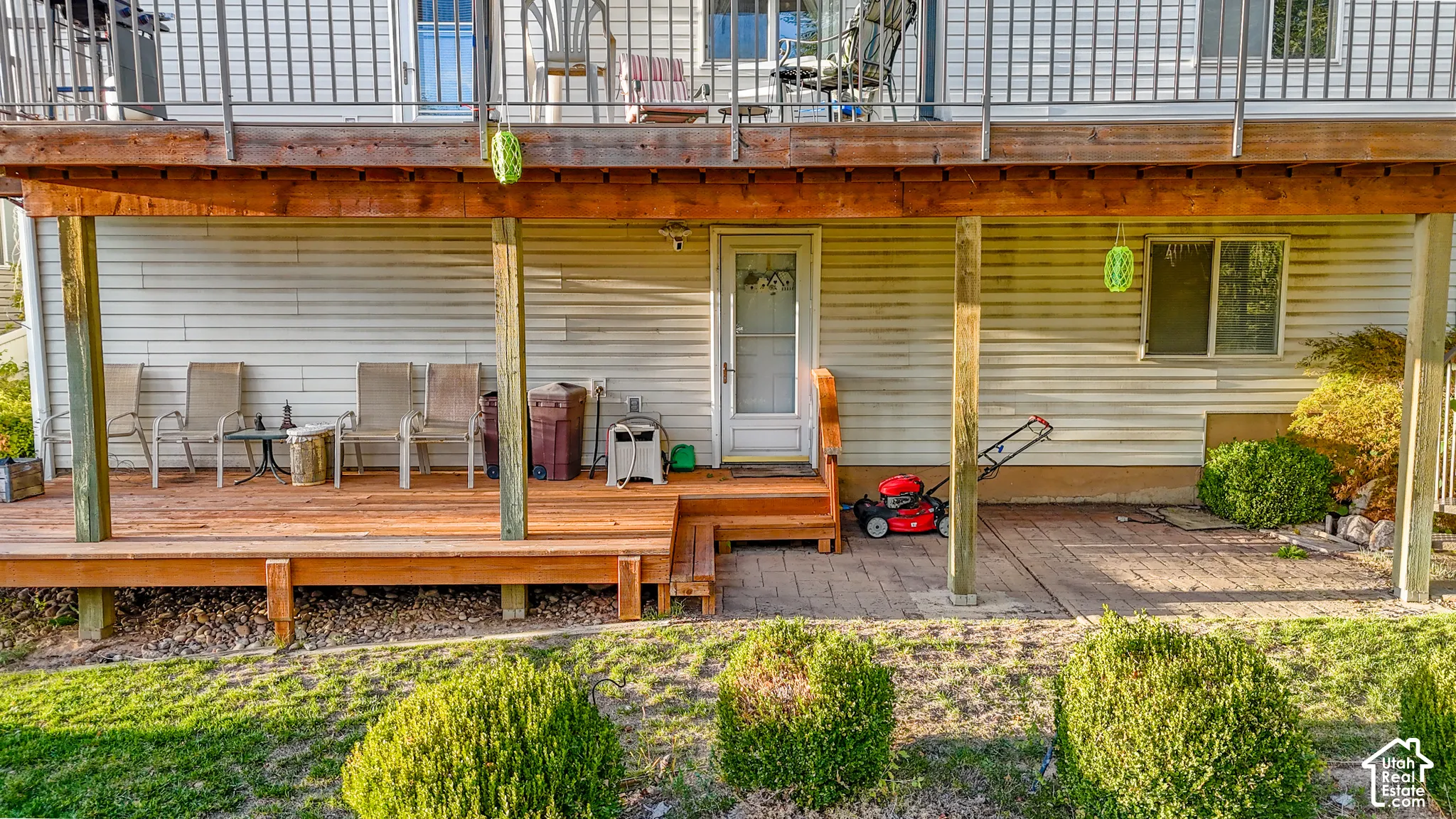 Covered wooden deck featuring structural support posts, partial paver patio, and exterior door access