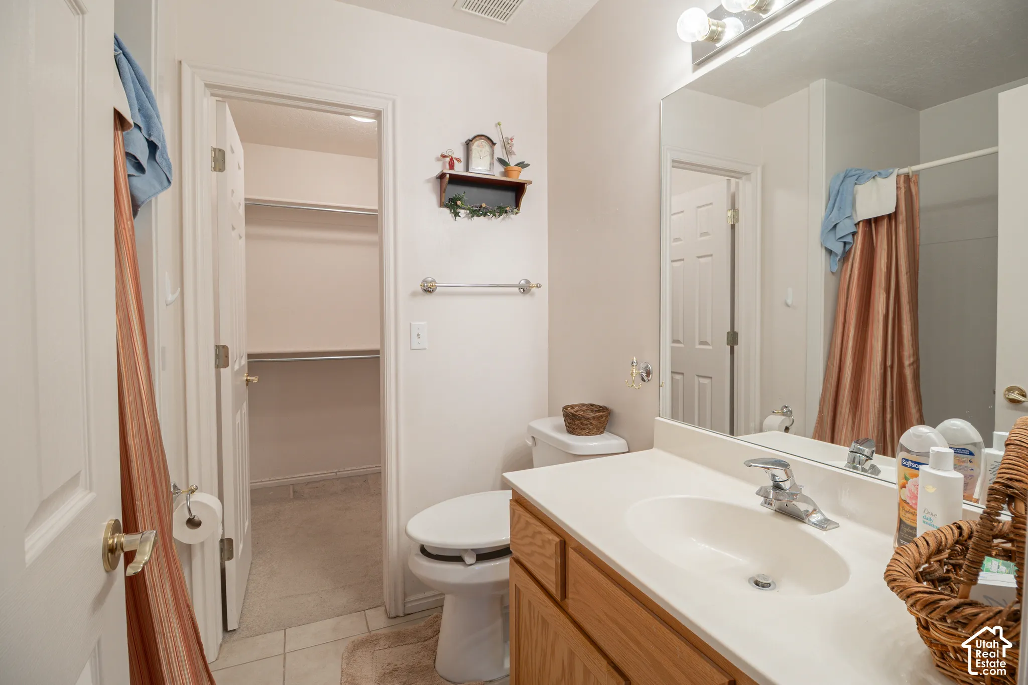 Bathroom featuring a wood-finish vanity with an integrated sink, large wall-mounted mirror, chrome fixtures, and a walk-in closet