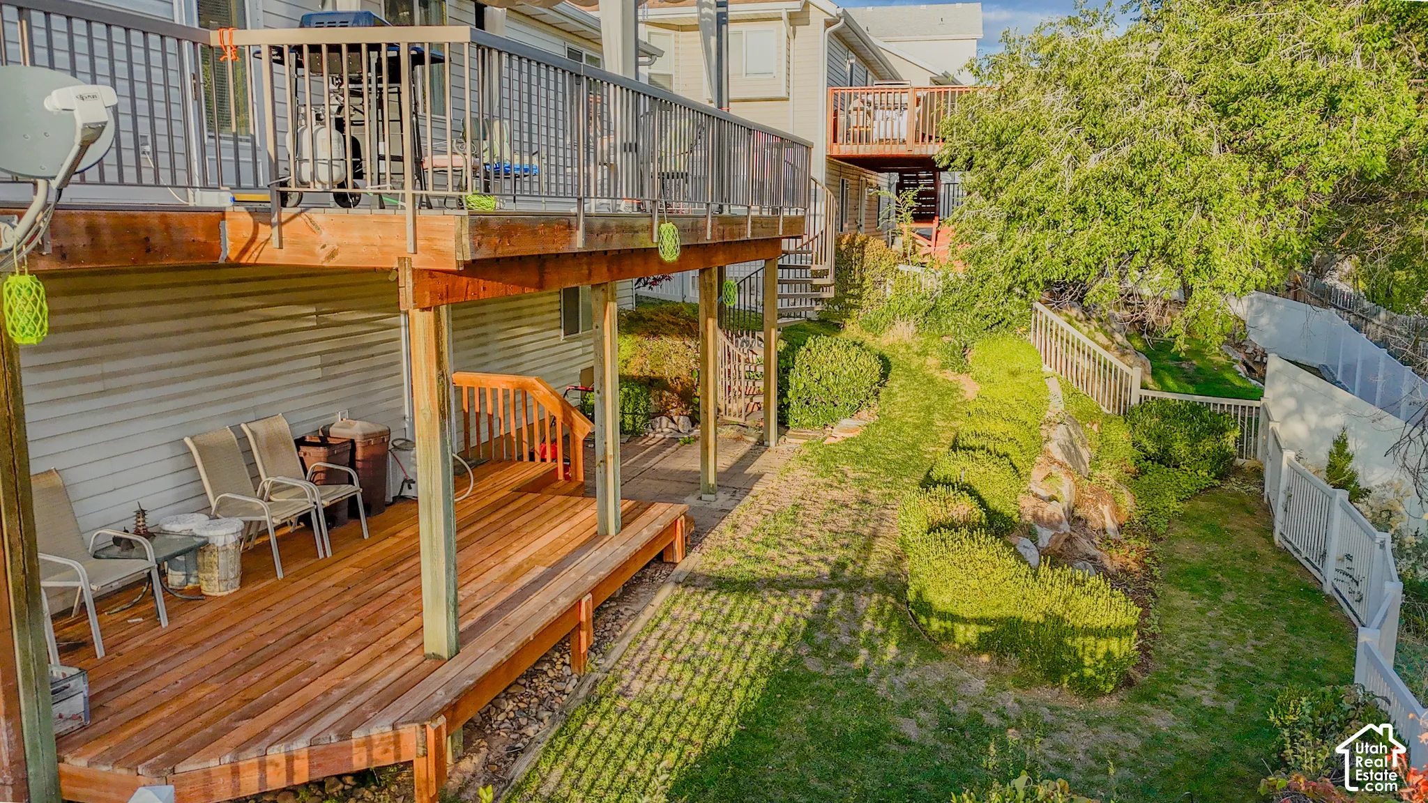 Multi-level wood decking with metal railing, covered patio space, manicured landscaping, and perimeter fencing