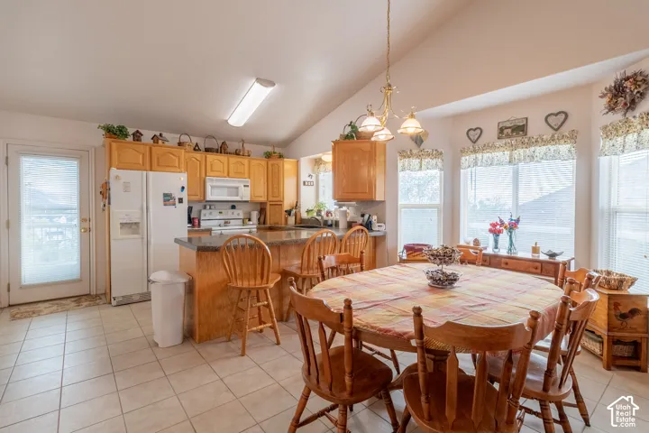 Kitchen featuring natural wood cabinetry, a peninsula with bar seating, tiled flooring, vaulted ceilings, and large multi-pane windows