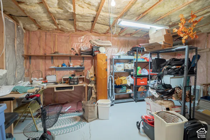 Utility area featuring exposed joist ceiling, fiberglass wall insulation, built-in wooden shelving, and painted concrete flooring