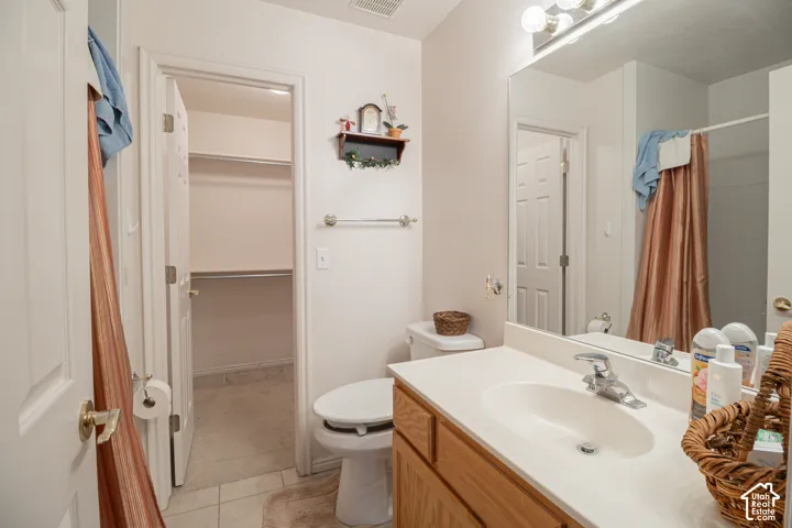 Bathroom featuring a wood-finish vanity with an integrated sink, large wall-mounted mirror, chrome fixtures, and a walk-in closet