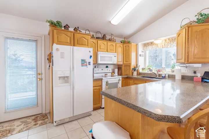 Kitchen featuring solid wood cabinetry, stone-composite countertops, a peninsula with bar seating, tile flooring, and white built-in appliances