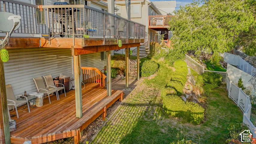 Multi-level wood decking with metal railing, covered patio space, manicured landscaping, and perimeter fencing