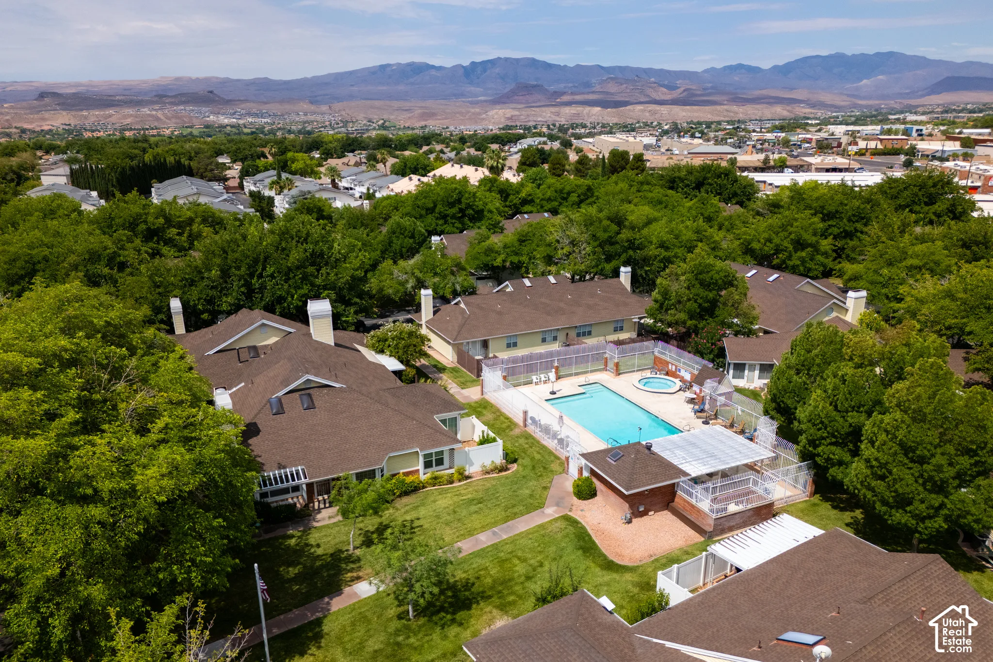 Aerial property perspective featuring a community swimming pool, a dedicated spa, a shaded patio structure, and mature landscaping set against a mountain backdrop