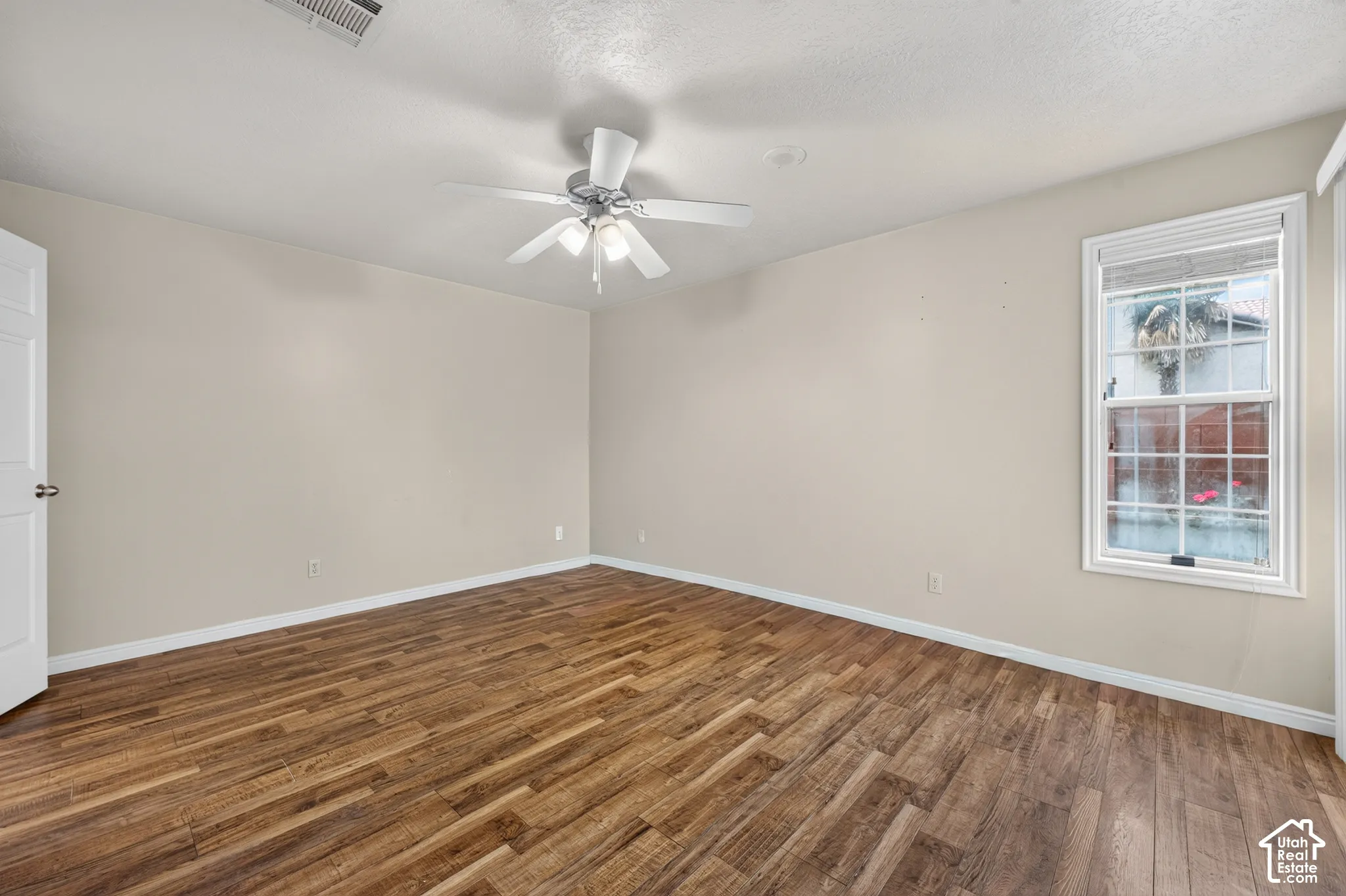 Interior room featuring wood-finish flooring, a multi-blade ceiling fan with integrated lighting, and a window with a multi-pane grid design