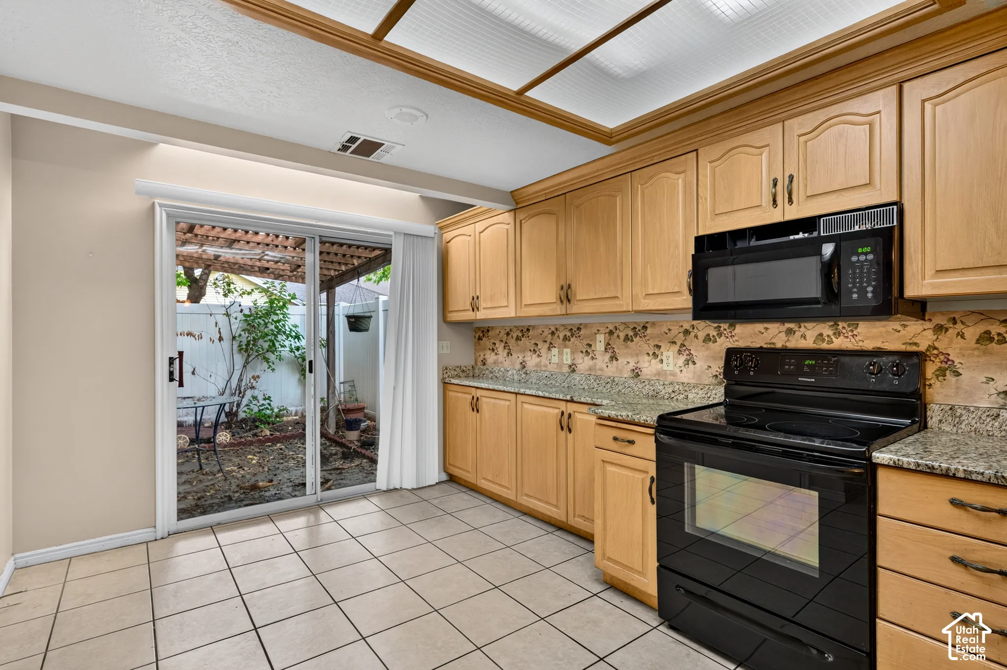 Kitchen featuring light-finish cabinetry, stone-style countertops, built-in black appliances, recessed tray ceiling, and ceramic tile flooring
