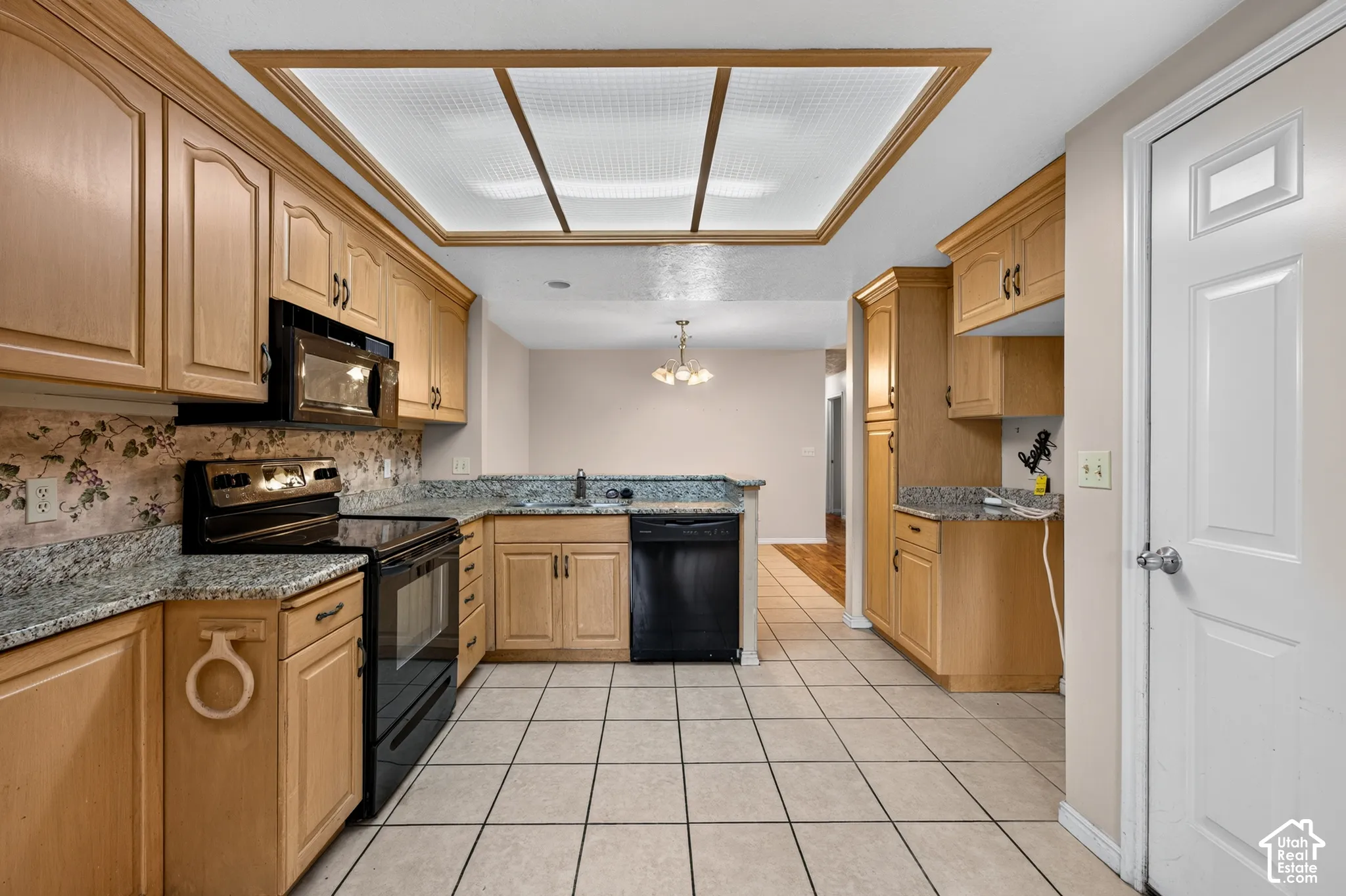 Kitchen featuring natural wood cabinetry, stone-finish countertops, black built-in appliances, a large recessed light fixture, and ceramic tile flooring