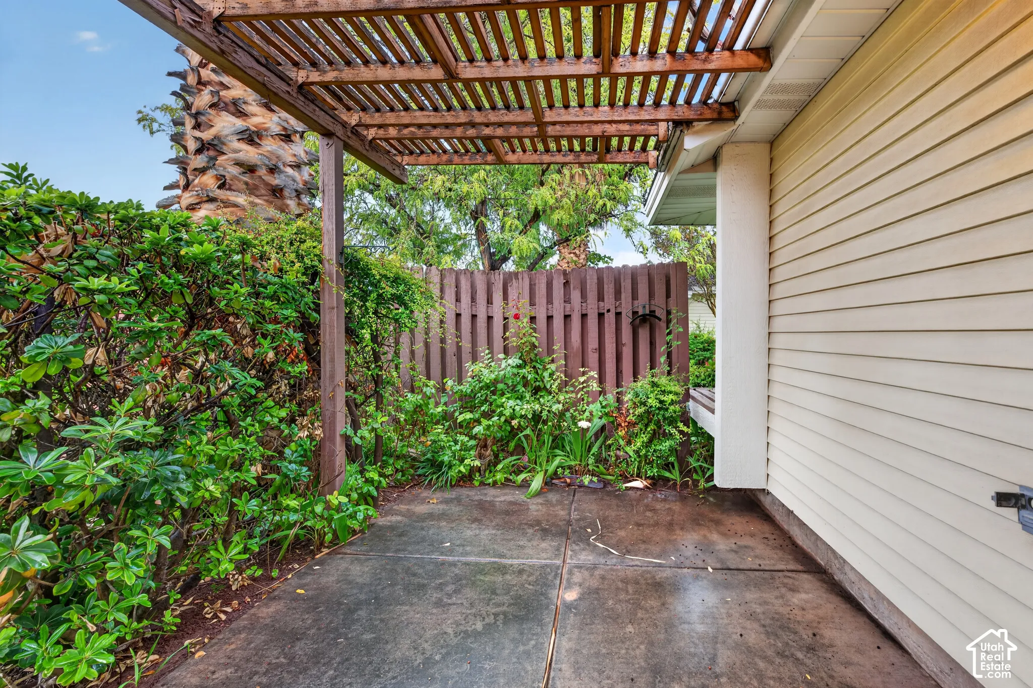 Concrete patio area featuring a wooden pergola, privacy fencing, and exterior lap siding