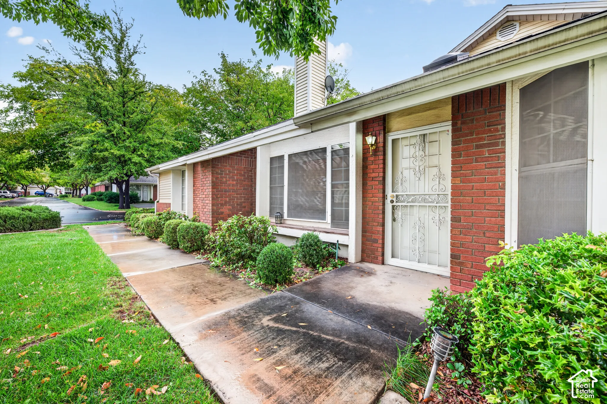 Exterior facade featuring red brick masonry, a metal screen entry door, multi-pane windows, and concrete walkway
