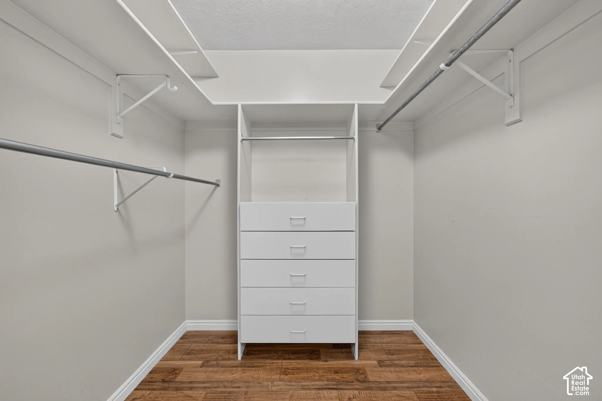 Walk-in closet featuring wood-finish flooring, built-in five-drawer chest, upper shelving, and dual hanging rods