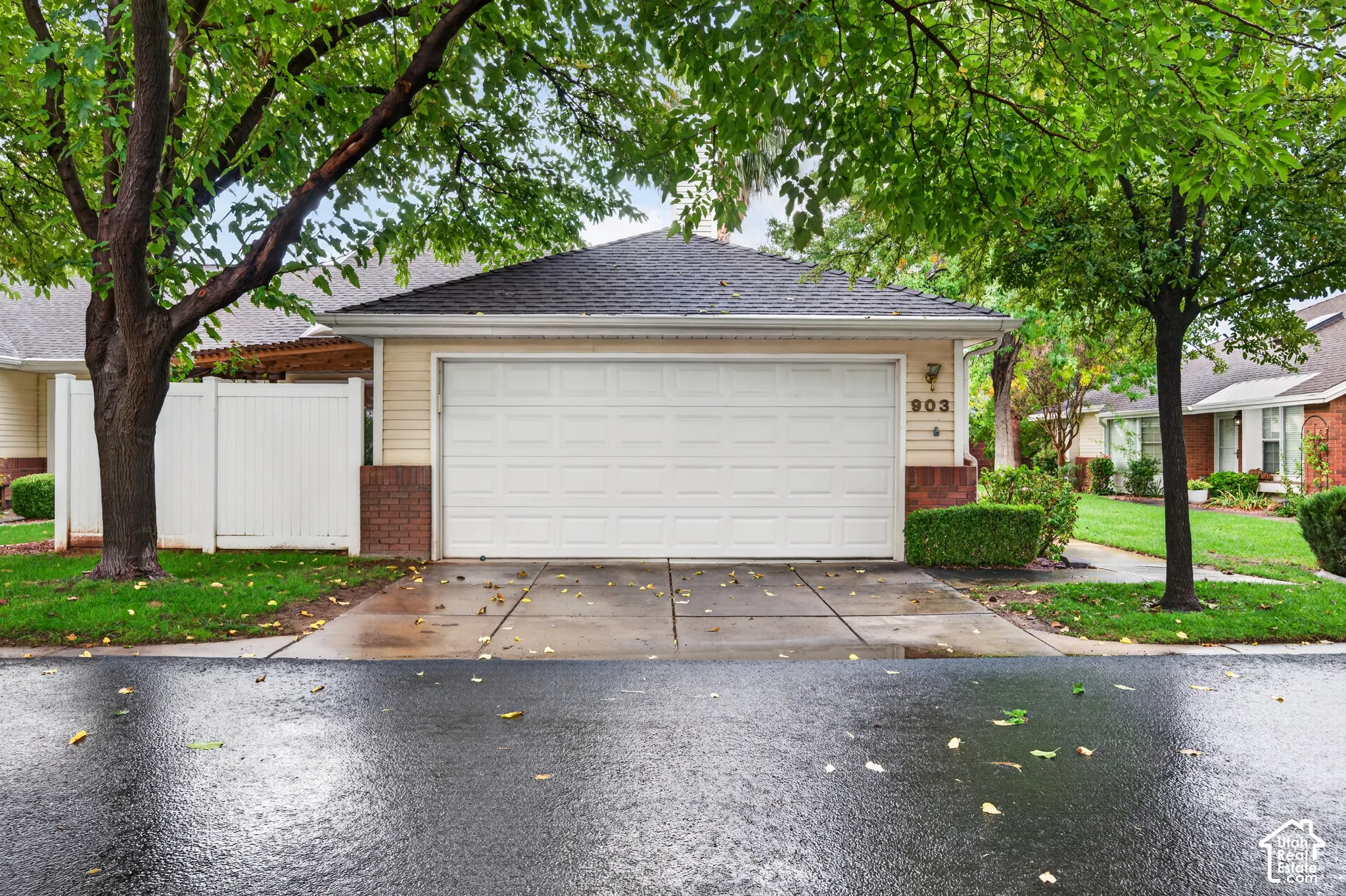 Two-car garage featuring a shingle roof, lap siding, and brick-veneer accents, paired with a concrete driveway and white vinyl fencing