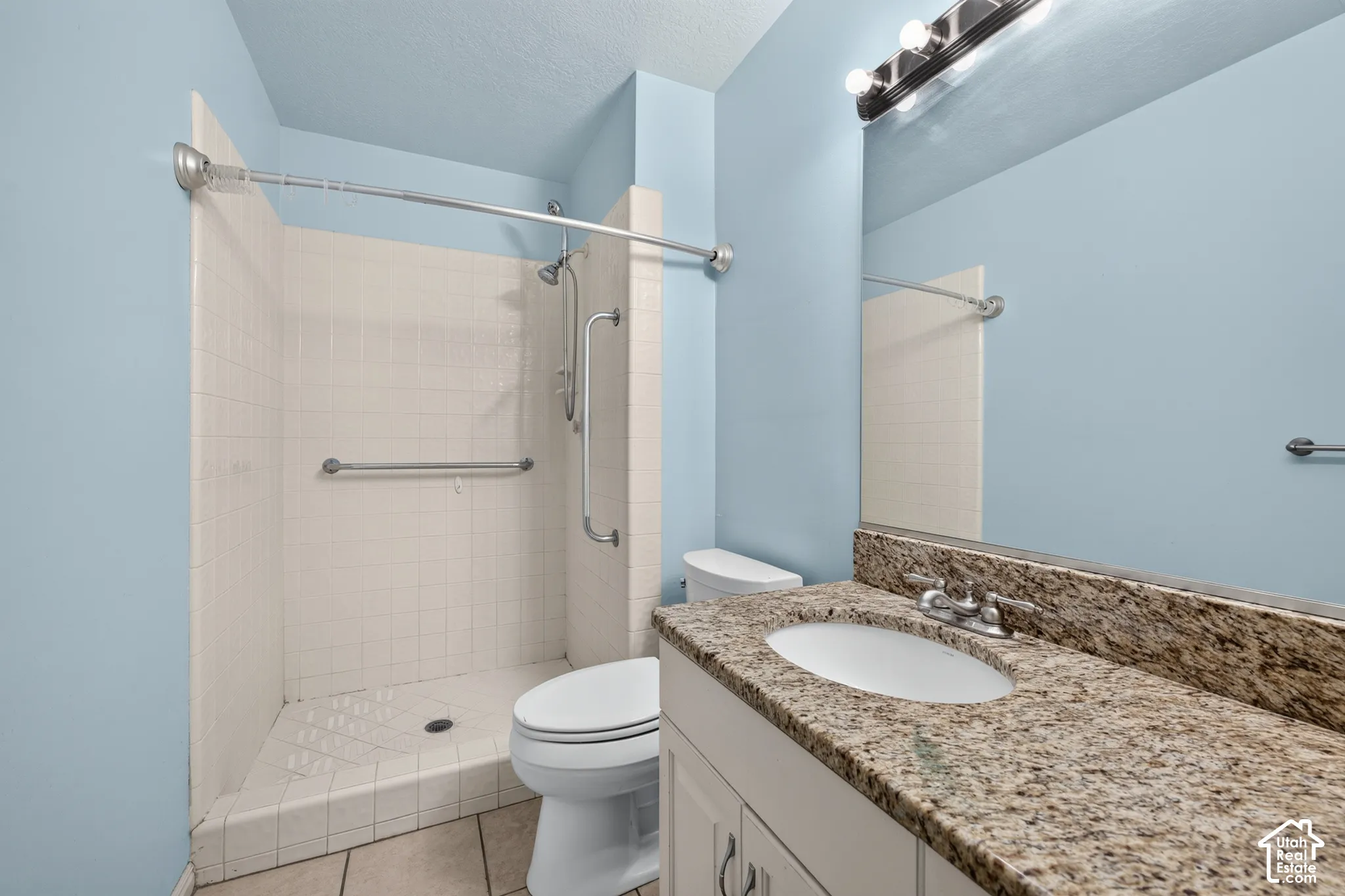 Bathroom featuring a vanity with stone-finish countertop and undermount sink, large wall mirror, and walk-in shower with tile surround