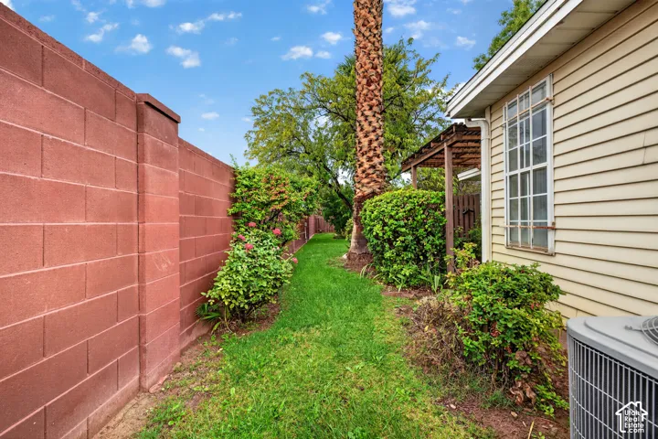 Side yard featuring a masonry block wall, exterior siding, mature landscaping, and a wood-slat pergola