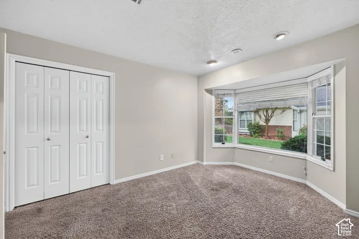 Bay window with multi-pane glass, bi-fold closet doors, recessed lighting, and neutral carpeting