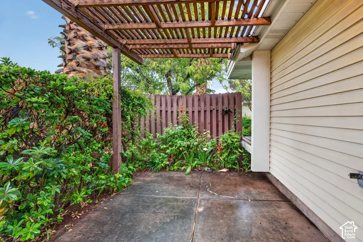 Concrete patio area featuring a wooden pergola, privacy fencing, and exterior lap siding