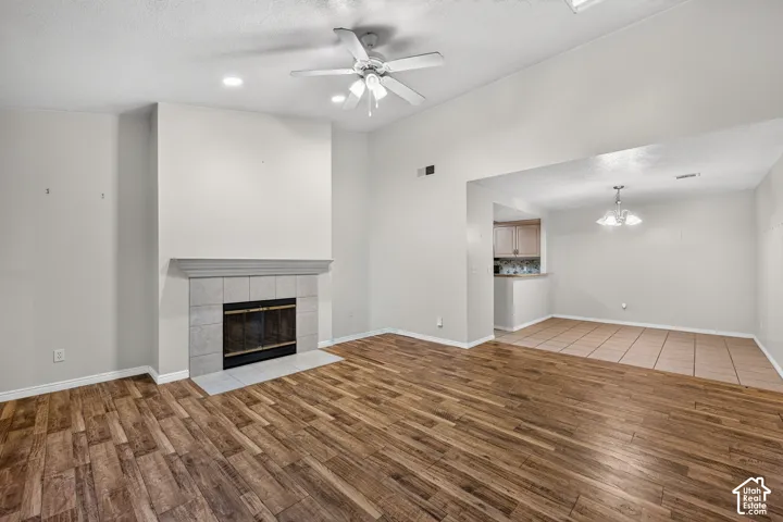 Vaulted ceilings with a central fan, fireplace with a stone-surround mantle, wood-finish flooring, recessed lighting, and tile flooring in the secondary area