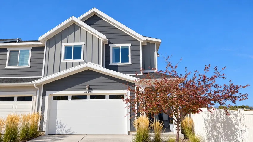 Multi-level exterior featuring dark horizontal and vertical siding, crisp white trim, a double-car garage with transom windows, and a paved driveway
