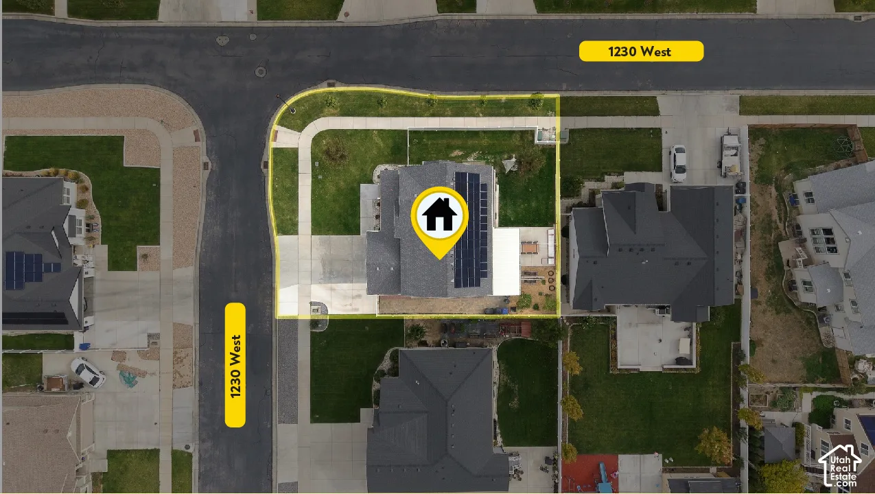 Corner lot featuring a paved driveway, solar panel array, and a concrete patio